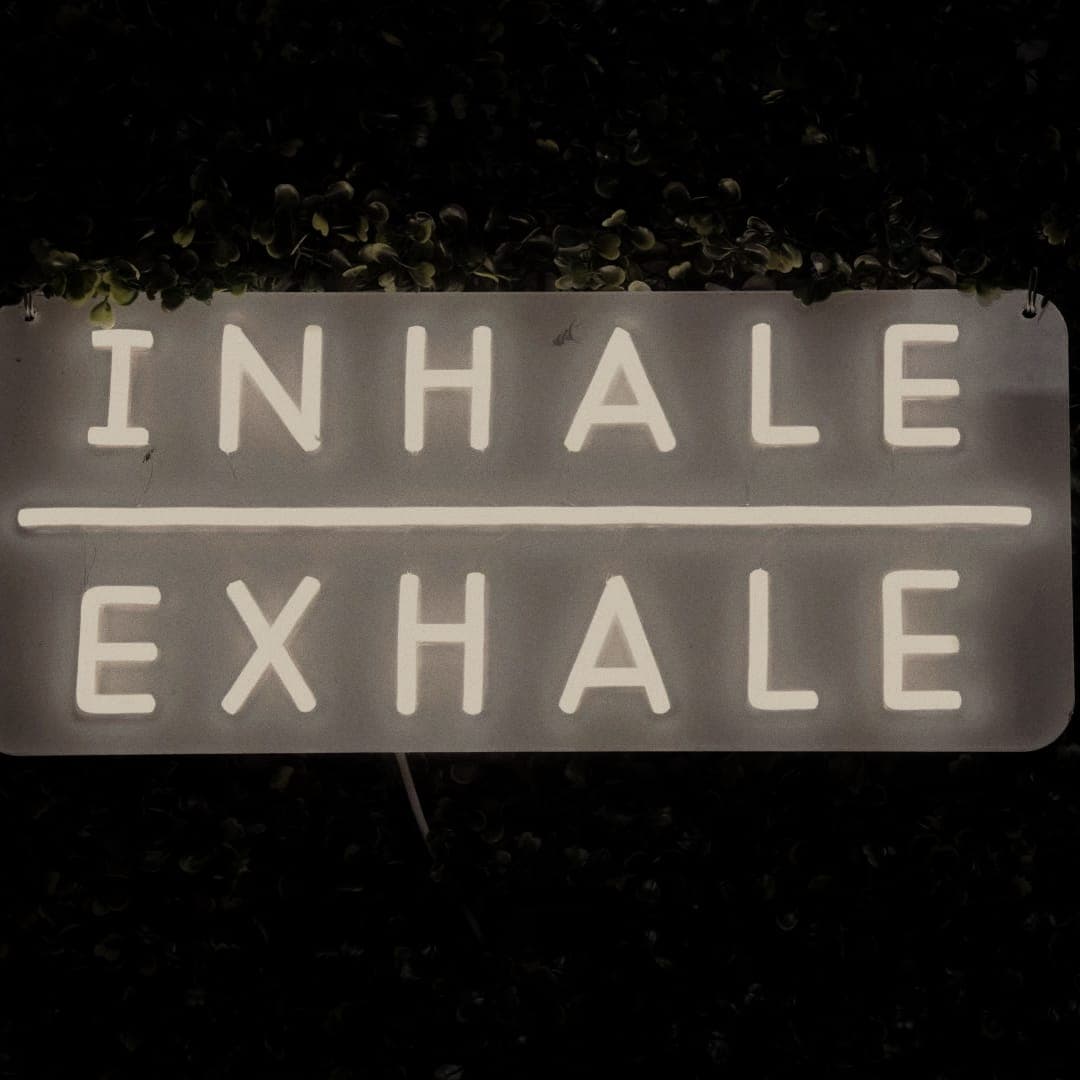 Inhale Exhale neon sign on a living green wall at The Den